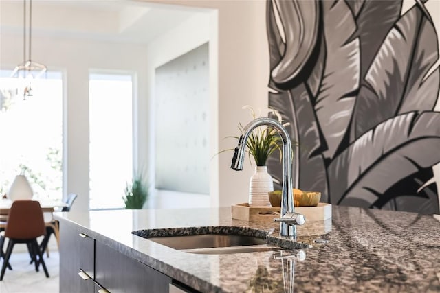 kitchen with dark stone counters, a tray ceiling, dark cabinetry, pendant lighting, and a sink