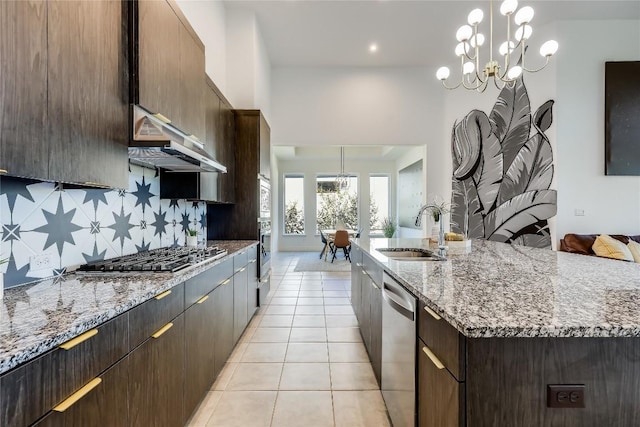 kitchen featuring light tile patterned floors, a kitchen island with sink, under cabinet range hood, stainless steel appliances, and a sink