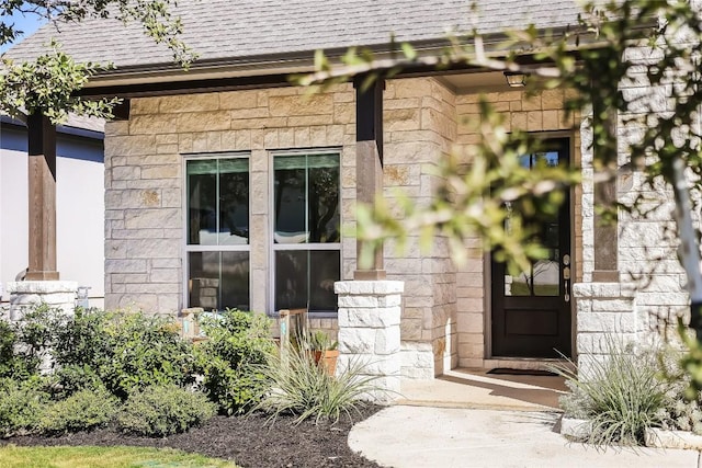 entrance to property with stone siding and a shingled roof