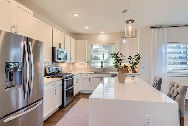 kitchen with a center island, appliances with stainless steel finishes, white cabinets, decorative light fixtures, and sink