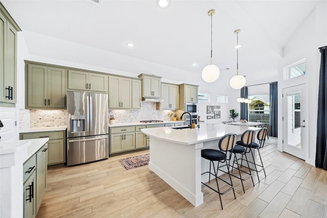 kitchen with a center island with sink, sink, appliances with stainless steel finishes, decorative light fixtures, and a breakfast bar area