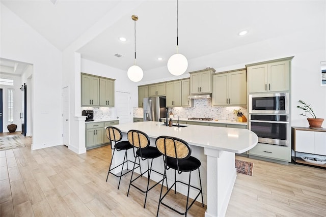 kitchen with a kitchen island with sink, a kitchen breakfast bar, decorative light fixtures, decorative backsplash, and appliances with stainless steel finishes