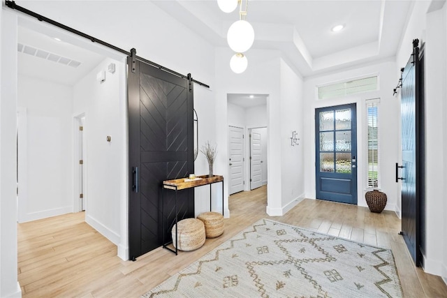 foyer featuring light hardwood / wood-style floors, a barn door, and a tray ceiling