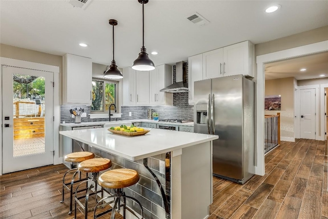 kitchen with wall chimney range hood, decorative light fixtures, white cabinets, stainless steel fridge with ice dispenser, and a kitchen island