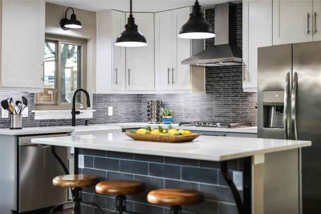 kitchen featuring wall chimney range hood, hanging light fixtures, decorative backsplash, white cabinetry, and stainless steel appliances