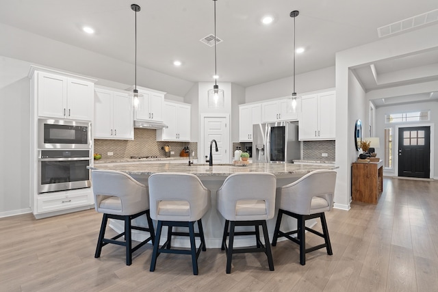 kitchen with decorative light fixtures, a large island with sink, a kitchen bar, stainless steel appliances, and white cabinets