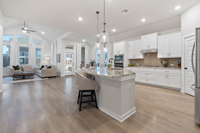 kitchen with lofted ceiling, pendant lighting, white cabinetry, and a center island with sink