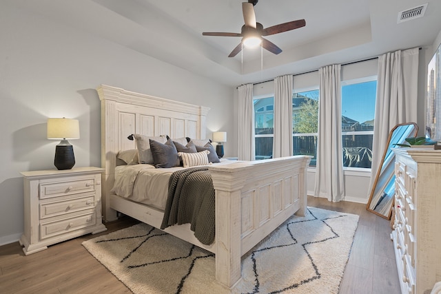 bedroom featuring a raised ceiling, light wood-type flooring, and ceiling fan