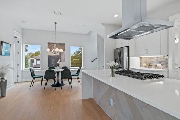 kitchen with stainless steel appliances, tasteful backsplash, decorative light fixtures, island range hood, and white cabinets