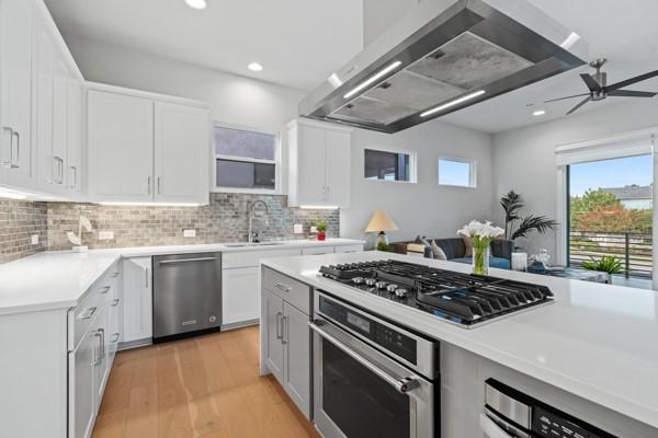 kitchen with white cabinets, wall chimney range hood, sink, decorative backsplash, and stainless steel appliances