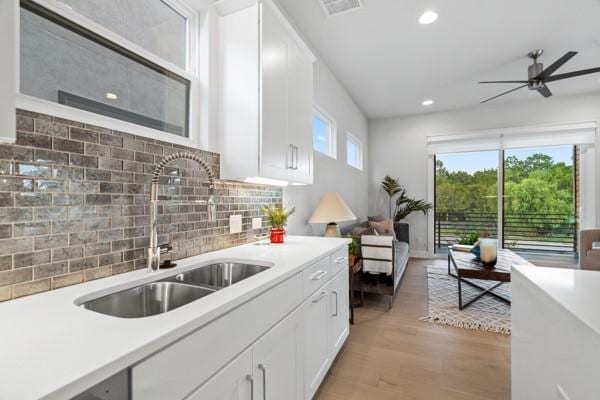 kitchen with backsplash, light hardwood / wood-style floors, white cabinetry, and sink