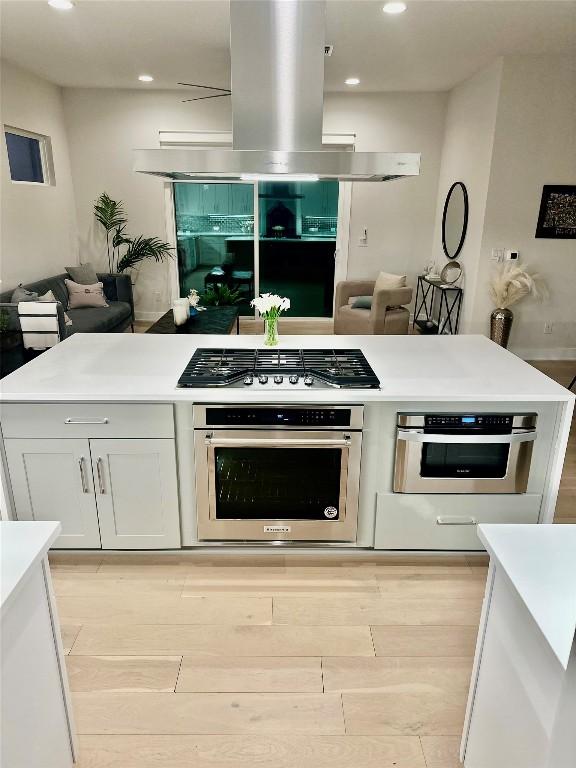 kitchen featuring island range hood, white cabinetry, appliances with stainless steel finishes, and light hardwood / wood-style flooring