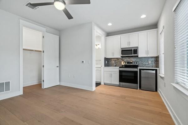 kitchen with decorative backsplash, appliances with stainless steel finishes, ceiling fan, light hardwood / wood-style floors, and white cabinetry