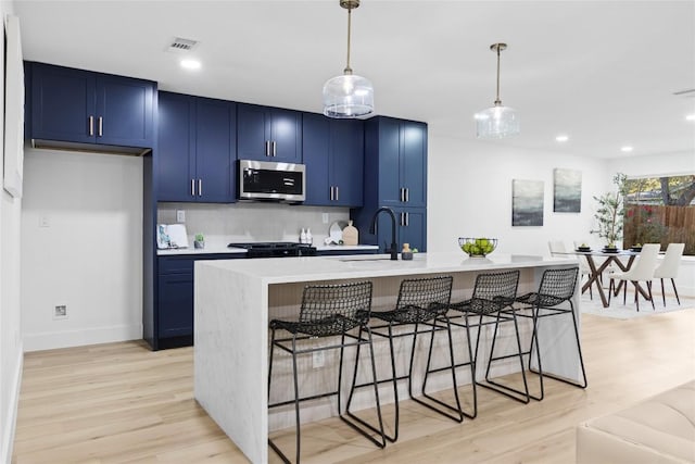 kitchen featuring pendant lighting, blue cabinets, sink, an island with sink, and a kitchen bar