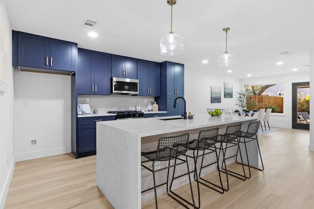 kitchen featuring a kitchen bar, sink, blue cabinets, and an island with sink