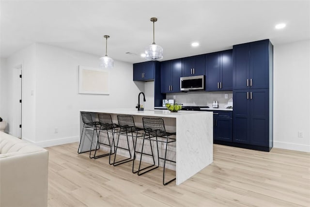 kitchen with blue cabinets, an island with sink, pendant lighting, a breakfast bar area, and light wood-type flooring