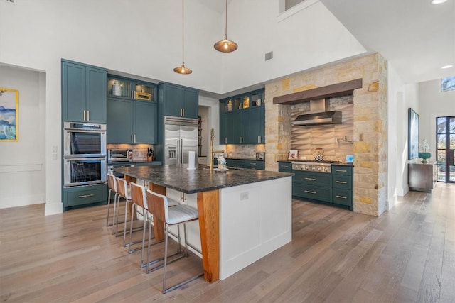 kitchen featuring decorative backsplash, appliances with stainless steel finishes, a kitchen bar, a kitchen island with sink, and hanging light fixtures