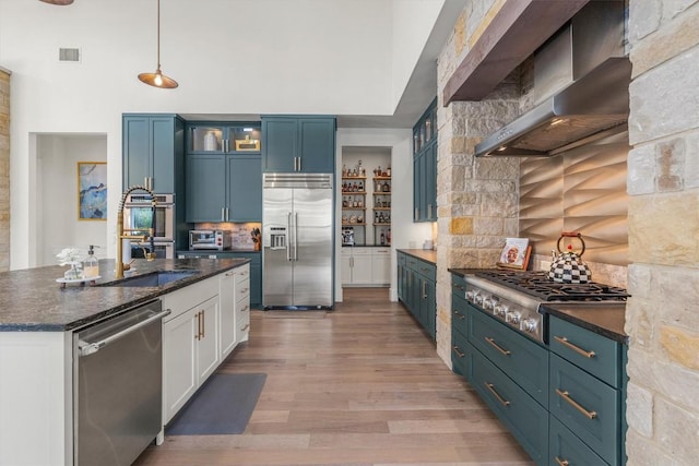 kitchen with wall chimney exhaust hood, blue cabinets, light hardwood / wood-style floors, decorative light fixtures, and appliances with stainless steel finishes