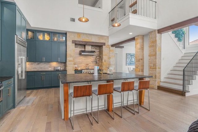 kitchen with hanging light fixtures, light hardwood / wood-style flooring, a towering ceiling, blue cabinetry, and tasteful backsplash