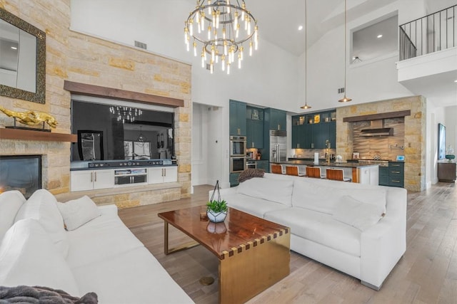 living room featuring a fireplace, high vaulted ceiling, an inviting chandelier, and light wood-type flooring