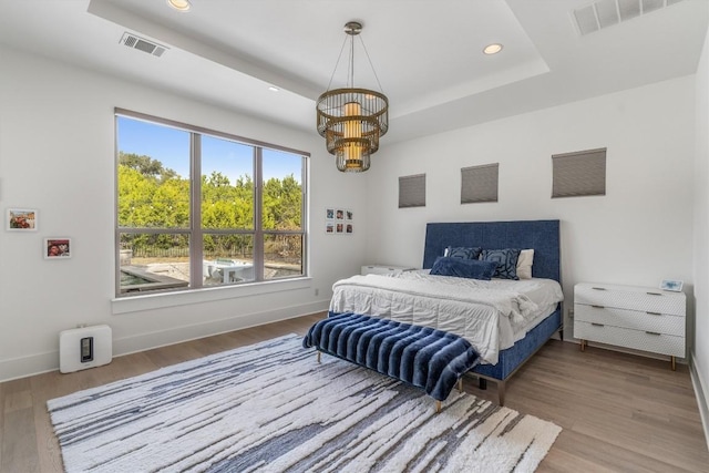 bedroom with a tray ceiling, multiple windows, hardwood / wood-style floors, and an inviting chandelier