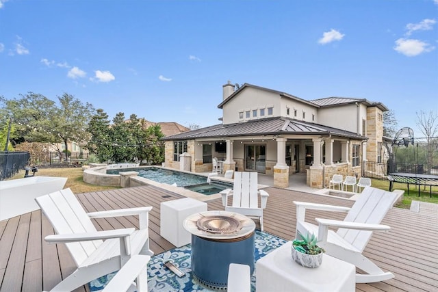 wooden terrace featuring a fire pit, a trampoline, an outdoor kitchen, a pool with hot tub, and a patio