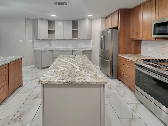 kitchen with decorative backsplash, light stone counters, a kitchen island, and appliances with stainless steel finishes