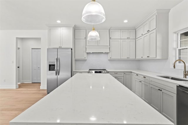 kitchen featuring light wood-type flooring, light stone counters, stainless steel appliances, sink, and decorative light fixtures