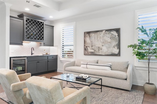 living room featuring light hardwood / wood-style flooring, wet bar, beverage cooler, and crown molding