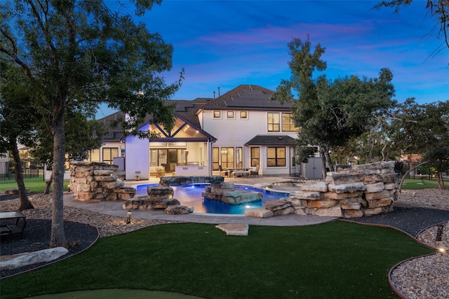 back house at dusk with a patio area, pool water feature, a yard, and solar panels