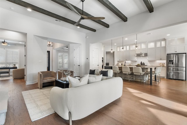 living room featuring ceiling fan, hardwood / wood-style floors, beamed ceiling, and a healthy amount of sunlight