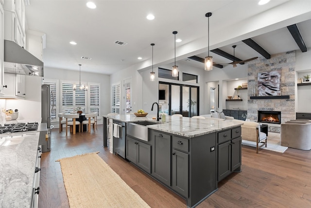 kitchen with beamed ceiling, decorative light fixtures, white cabinets, and a kitchen island with sink