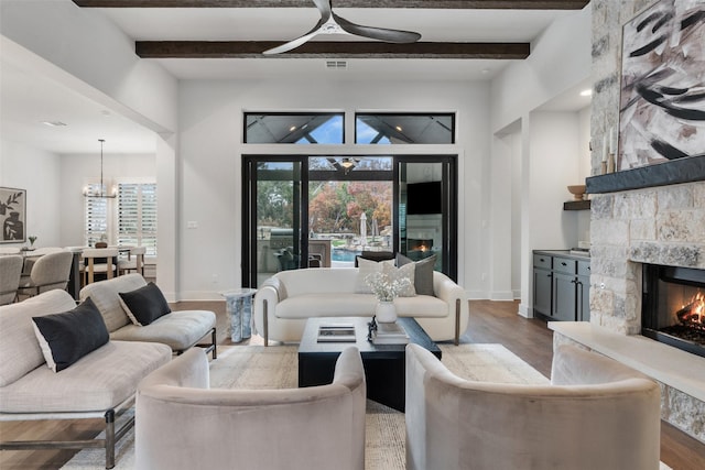 living room featuring beamed ceiling, ceiling fan with notable chandelier, light hardwood / wood-style flooring, and a stone fireplace