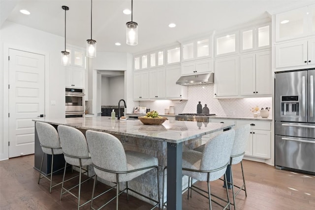 kitchen with light stone countertops, appliances with stainless steel finishes, a breakfast bar, a center island with sink, and white cabinetry