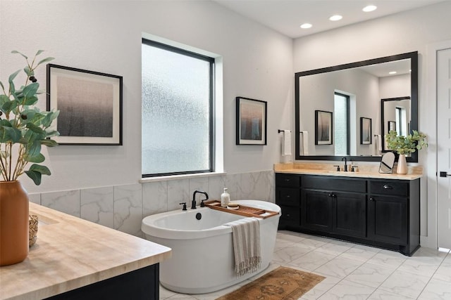 bathroom with a washtub, vanity, and tile walls