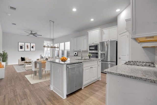 kitchen with white cabinets, pendant lighting, stainless steel appliances, and an island with sink