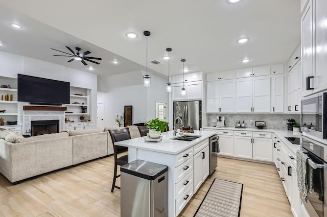 kitchen featuring appliances with stainless steel finishes, decorative light fixtures, white cabinetry, an island with sink, and sink