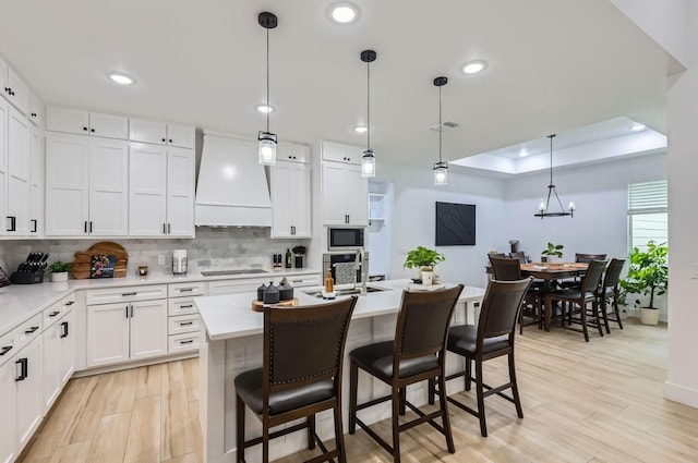 kitchen featuring built in microwave, white cabinetry, a raised ceiling, and premium range hood