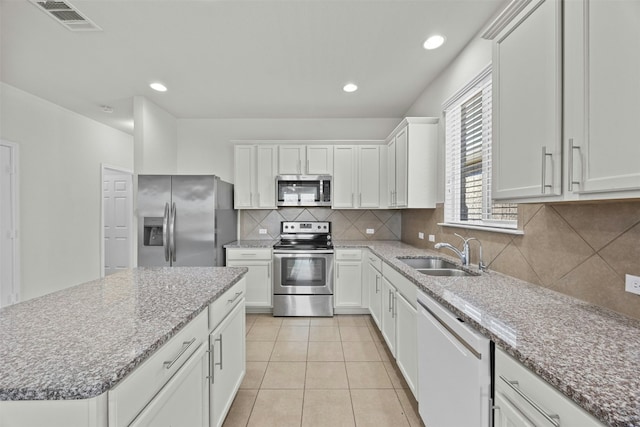 kitchen with backsplash, sink, light stone countertops, white cabinetry, and stainless steel appliances