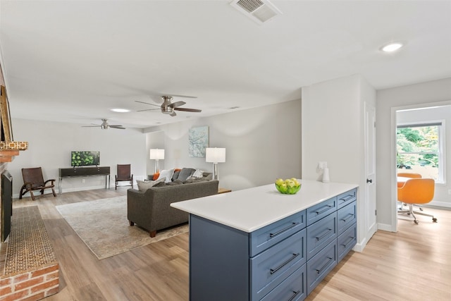 kitchen featuring blue cabinetry, light hardwood / wood-style flooring, ceiling fan, and a fireplace