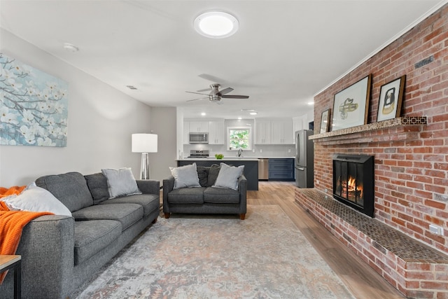 living room featuring a fireplace, ceiling fan, sink, and light wood-type flooring