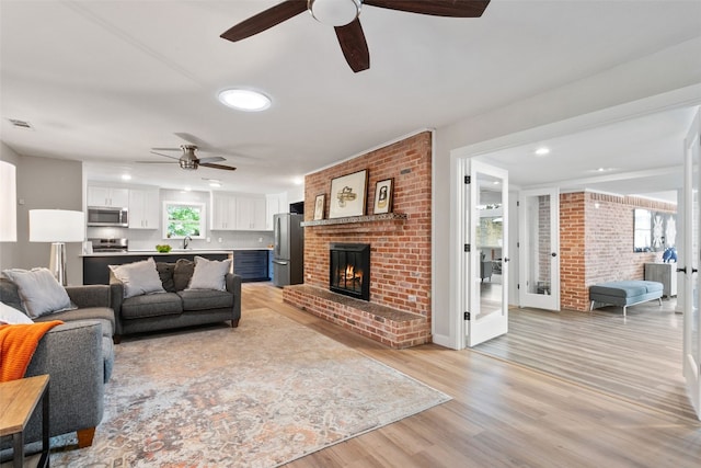 living room with a fireplace, ceiling fan, sink, and light hardwood / wood-style floors