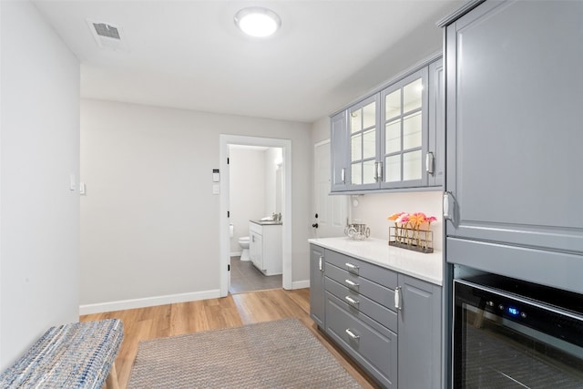 kitchen with light wood-type flooring, beverage cooler, and gray cabinetry