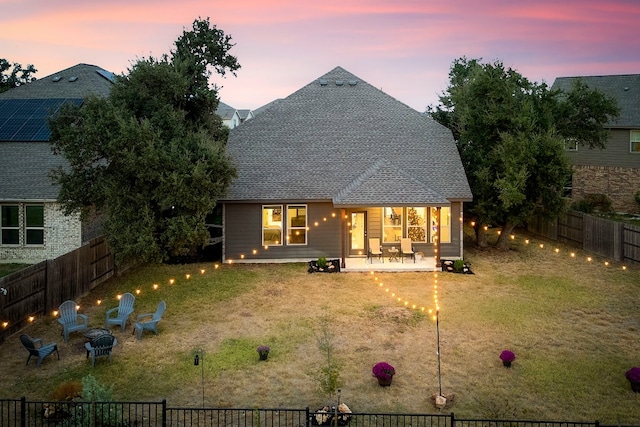 back house at dusk with a patio and a yard