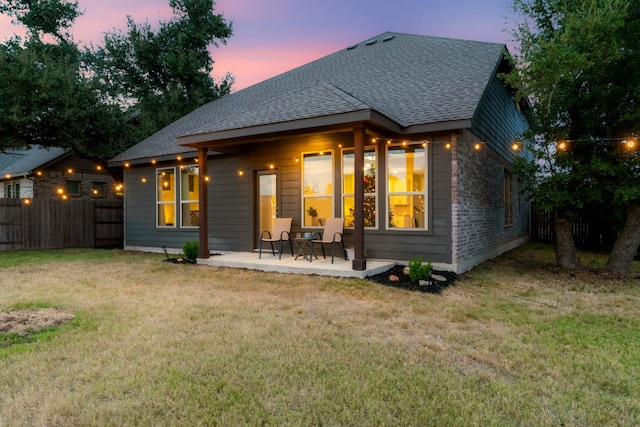 back house at dusk featuring a patio and a yard