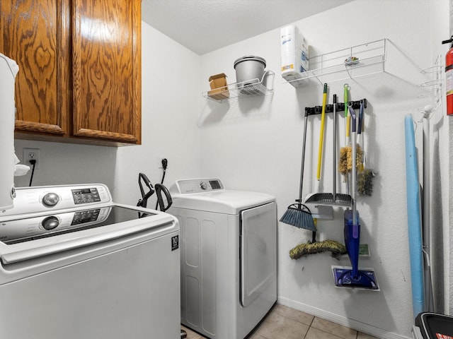 clothes washing area with washer and dryer, cabinets, and light tile patterned floors