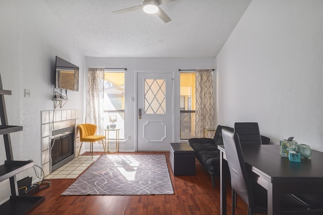 interior space featuring wood-type flooring, a textured ceiling, ceiling fan, and a tiled fireplace