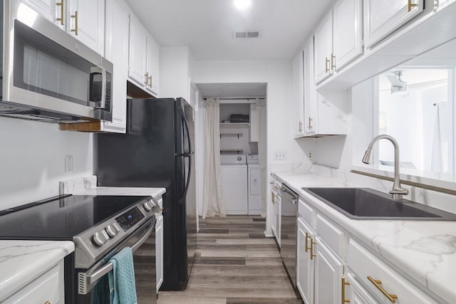 kitchen featuring sink, independent washer and dryer, appliances with stainless steel finishes, light stone counters, and white cabinetry