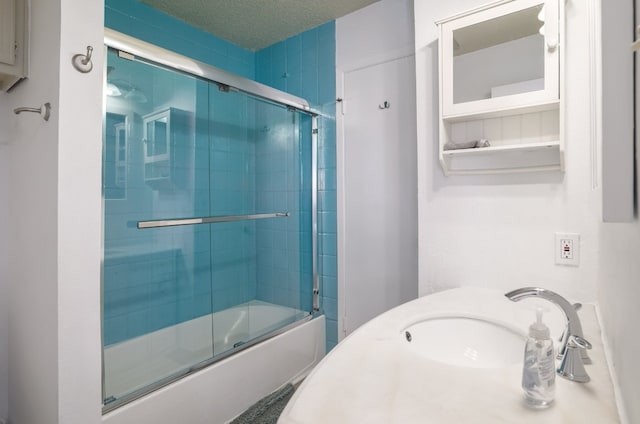 bathroom with a textured ceiling, shower / bath combination with glass door, and sink