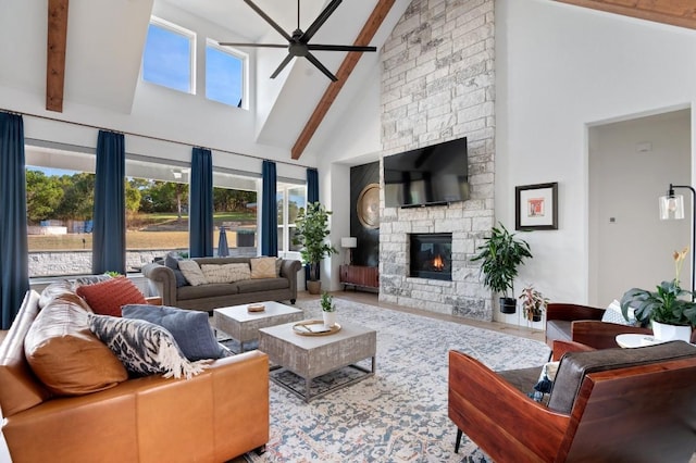 living room featuring a stone fireplace, ceiling fan, beamed ceiling, and high vaulted ceiling